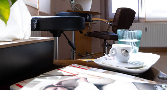 Zeitschriften, Kaffe, Wasser und ein Friseursessel sowie Spiegel im Bild.